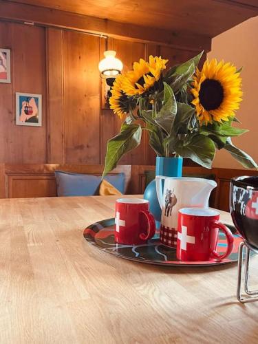 a table with cups and a vase with sunflowers at Ferme Pasquier - Farmhouse with panoramic view - 1000 m2 garden in Avry devant Pont