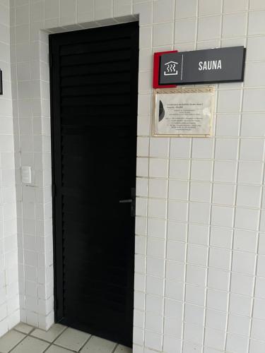 a black door in a white tiled wall with a sign at Life Flats Temporada com Bela vista à 50m da Praia in Recife