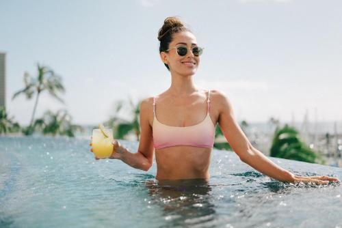 a woman in a bikini holding a drink in the water at Prince Waikiki in Honolulu