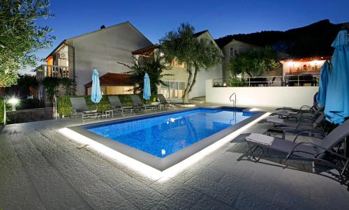 a swimming pool with chairs and umbrellas next to a house at Apartments Šemper - HEATED POOL in Bol