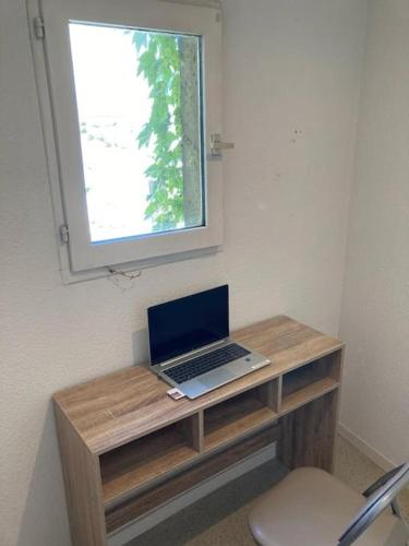 un ordinateur portable posé sur un bureau en bois sous une fenêtre dans l'établissement Appartement 1 cosy dans le centre, à Limoges