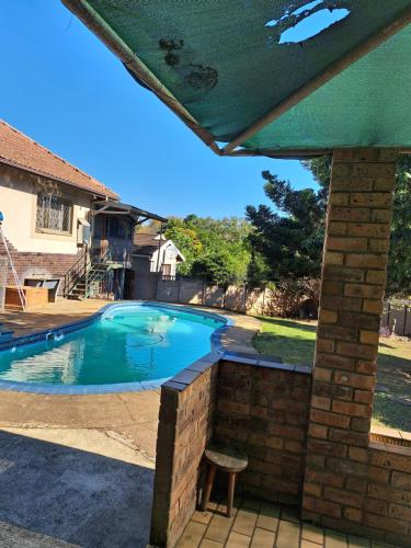 a swimming pool in a backyard with a green umbrella at PMB Backpackers Lodge in Pietermaritzburg