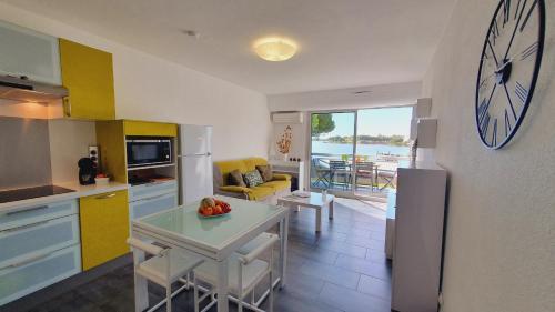 d'une cuisine et d'un salon avec une horloge murale. dans l'établissement L'OLYMPE VUE LAC PARKING CLIM WIFI - ROSSIconciergerie - Linge inclus, à La Grande Motte