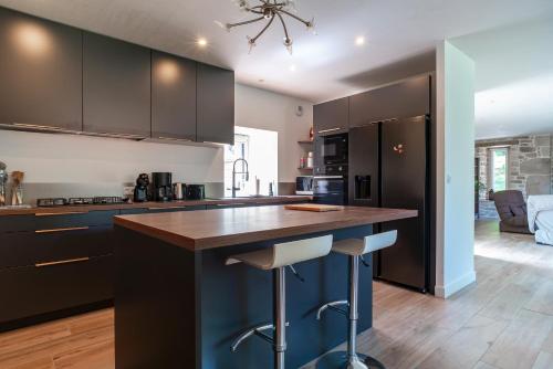 une cuisine avec des placards noirs et un comptoir avec des tabourets dans l'établissement Le Paradis Perdu - Maison avec jardin paysagé, à Quistinic