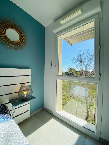 - une chambre dotée d'une grande fenêtre dans un mur bleu dans l'établissement Appart 4 pers climatisé parking piscine proche des plages ménage inclus - V0816, à Vias