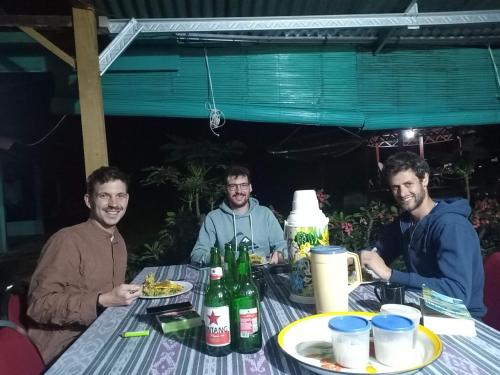 three men sitting at a table with food and drinks at Hobbit Hill in Ruteng