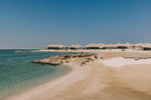 a beach with a bunch of umbrellas and the ocean at Our Habitas Ras Abrouq in Dukhān