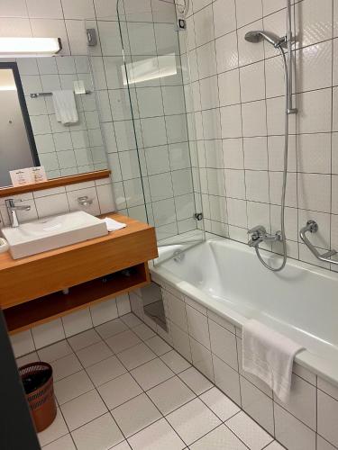 a bathroom with a tub and a sink and a mirror at Hotel Gasthof Krönele in Lustenau