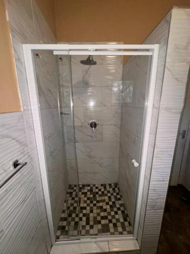 a shower with a glass door with a checkered floor at Falcon Lodge ET in Bela-Bela