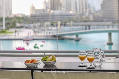 a table with two glasses of juice and a bowl of fruit at Manzil - Luxury 3BR Villa w/ maid room, Full Burj & Fountain view in Dubai