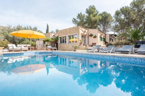 a swimming pool with an umbrella and chairs and a house at Casa Vista Monte in Llucmajor