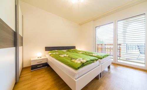a white bedroom with a bed with green sheets and a window at Residenz Ambassador B22 in Leukerbad