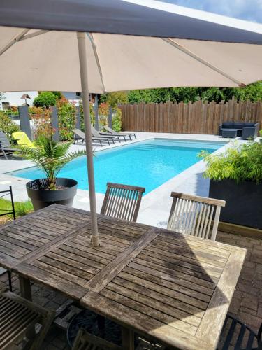 DalhundenにあるLogement privé dans une Villa avec piscineのスイミングプールの横にある木製テーブル(傘付)
