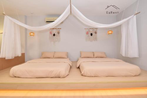 two beds in a room with white walls and curtains at Cozy Muji Studio Homestay near Taiping Lake Garden in Taiping