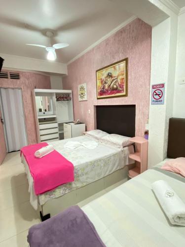 a bedroom with two beds and a pink wall at Suítes Sol do Guarujá in Guarujá