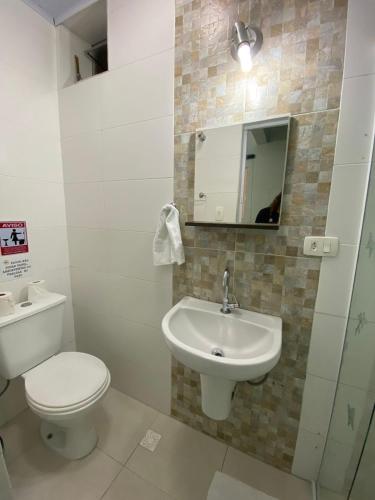 a bathroom with a toilet and a sink and a mirror at Suítes Sol do Guarujá in Guarujá