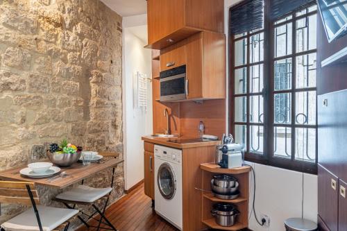 une cuisine avec lave-linge et sèche-linge à côté d'un mur en pierre dans l'établissement Lavie Maison little Flat Le Marais, à Paris
