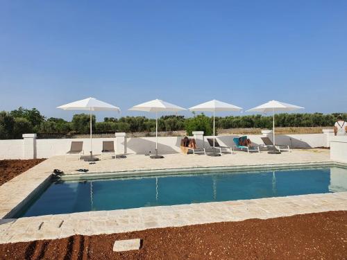 a swimming pool with white umbrellas and lounge chairs at Masseria Purgatorio in Fasano