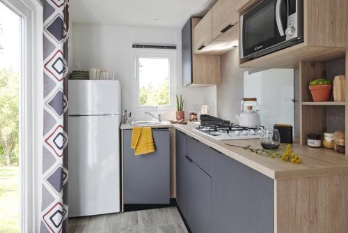 Il comprend une cuisine équipée d'un réfrigérateur blanc et d'une cuisinière. dans l'établissement Mobil home - Domaine du Vieux Moulin, à Saint-Julien-en-Born