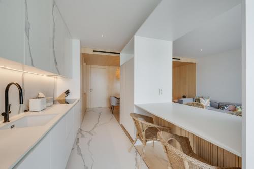 Una cocina con encimeras blancas, fregadero y sillas. en Chic Two-Bedroom En Suite in Central Town - Savoy Residence, en Funchal