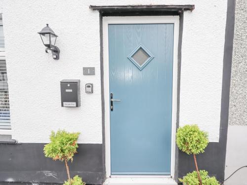 a blue door on a white house with two plants at Sea View Terrace in Conwy