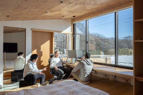 a group of people sitting around a desk in a room with windows at 森deワーケなすっぽ 木の温もりとホテルライクな佇まい 森のバレルサウナ in Nasu