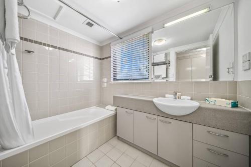a white bathroom with a sink and a tub and a bath tub at Perth city BNB l CBD and Pool view - 1xKing bed and 2xSingle beds in Perth