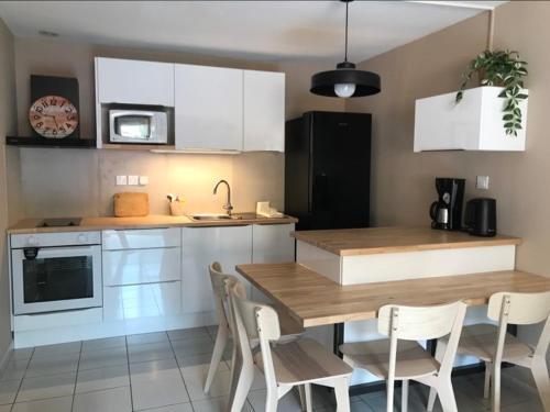 une cuisine avec des armoires blanches et une table et des chaises en bois dans l'établissement APPART 34 m2 - 300m de la plage - 4 pers - piscine - parking privé, à Narbonne-Plage