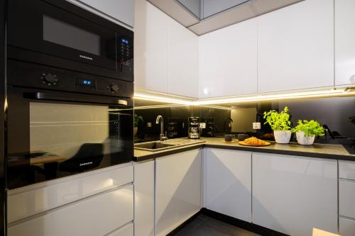 a kitchen with white cabinets and black appliances at Manufaktura Residence - Apartamenty Industrial z Parkingiem i Dwoma Łazienkami in Łódź