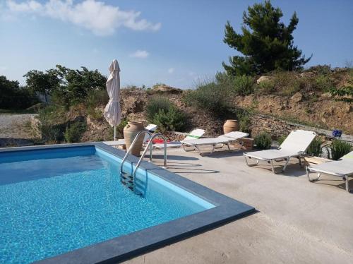 a swimming pool with chairs and an umbrella at Villa Vouno - luxury and privacy in the Aegean in Klíma
