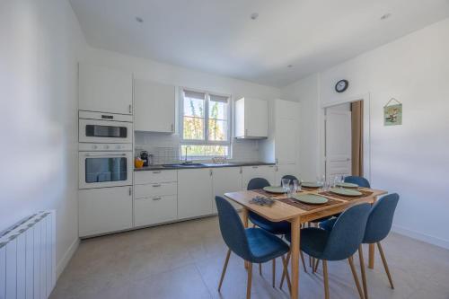 - une cuisine blanche avec une table en bois et des chaises bleues dans l'établissement La Maison du Fleuve - Welkeys, à Dives-sur-Mer