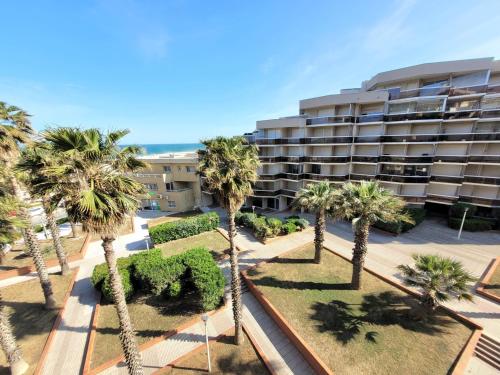 un immeuble avec des palmiers en face de celui-ci dans l'établissement Canet-en-Roussillon - Studio moderne pour 4 pers - Clim - Proche mer et commodités - FR-1-794-104, à Canet