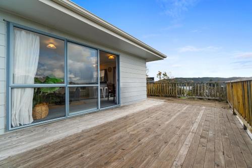 a home with a large deck with sliding glass doors at Raglan Beach Retreat - Raglan Holiday Home in Raglan