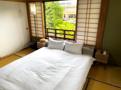 ein Schlafzimmer mit einem weißen Bett und einem Fenster in der Unterkunft 自然豊かな古民家豪邸 最大12名まで可 大人数に最適可で アクセス良好な 菱閣 in Fujikawaguchiko