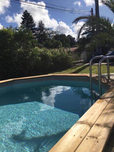 - une piscine avec une terrasse en bois et de l'eau bleue dans l'établissement Charmante Maison Entre Lac et Océan, à La Teste-de-Buch