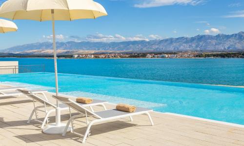 a swimming pool with two chairs and an umbrella at Aminess Style Glamping Villas & Holiday Homes Avalona in Povljana