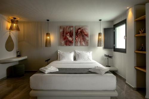 a bedroom with a large white bed with three paintings at Kudos Suites Firostefani in Fira