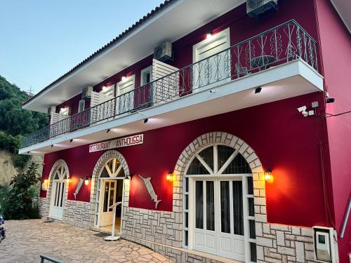 a red building with a balcony on top at Anthoussa Rooms in Parga