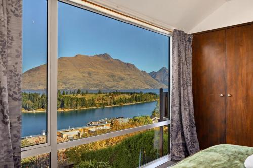 a bedroom with a large window with a view of a lake at Lake Views - Close to Town - Hot Tub - Spa Pool in Queenstown