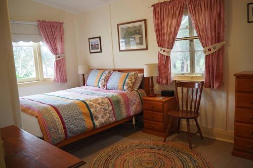 a bedroom with a bed and a chair and windows at Swallows Cottage, Margaret River in Witchcliffe