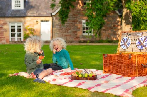 zwei Kinder sitzen auf einer Picknickdecke mit einem Obstkorb in der Unterkunft Balnagown Estates Gardener's Cottage in Kildary