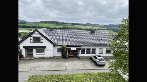 a white house with a car parked in the driveway at Bed & Breakfast Weisser Stein in Schmallenberg