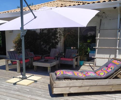 un parasol blanc sur une terrasse avec des chaises et des tables dans l'établissement Maison avec piscine chauffée entre océan et bassin, à Lège-Cap-Ferret