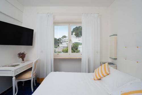 a white bedroom with a desk and a bed and a window at Sina Flora in Capri