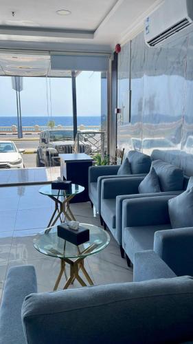 a living room with blue couches and tables and the ocean at Rose Land Hotel in Umm Lujj