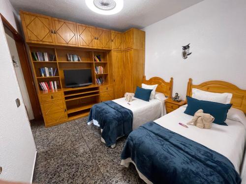 a bedroom with two beds and a tv and a book shelf at Vivienda Vacacional C & M in Puerto del Rosario