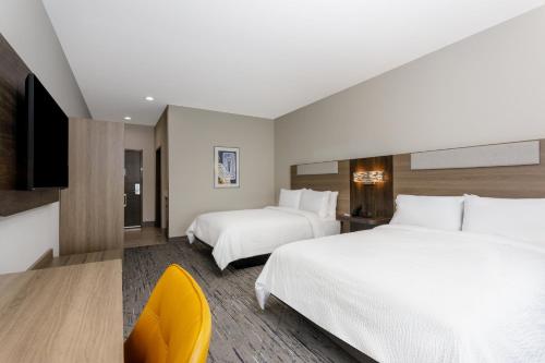 a hotel room with two beds and a yellow chair at Holiday Inn Express & Suites Tampa Stadium - Airport Area by IHG in Tampa