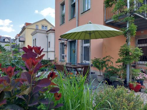 a patio with a table and an umbrella and flowers at Dein Zuhause in der Ferne im grünen Kreativhof "Der Gute Ton" mit kostenlosem Fahrradverleih in Dresden
