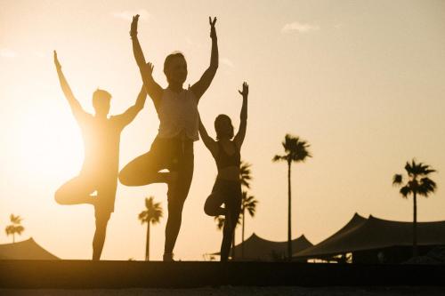 a group of people jumping on the beach at sunset at Our Habitas Ras Abrouq in Dukhān