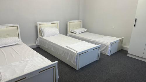 three beds in a room with white walls at Nazar Hotel & hostel in Türkistan